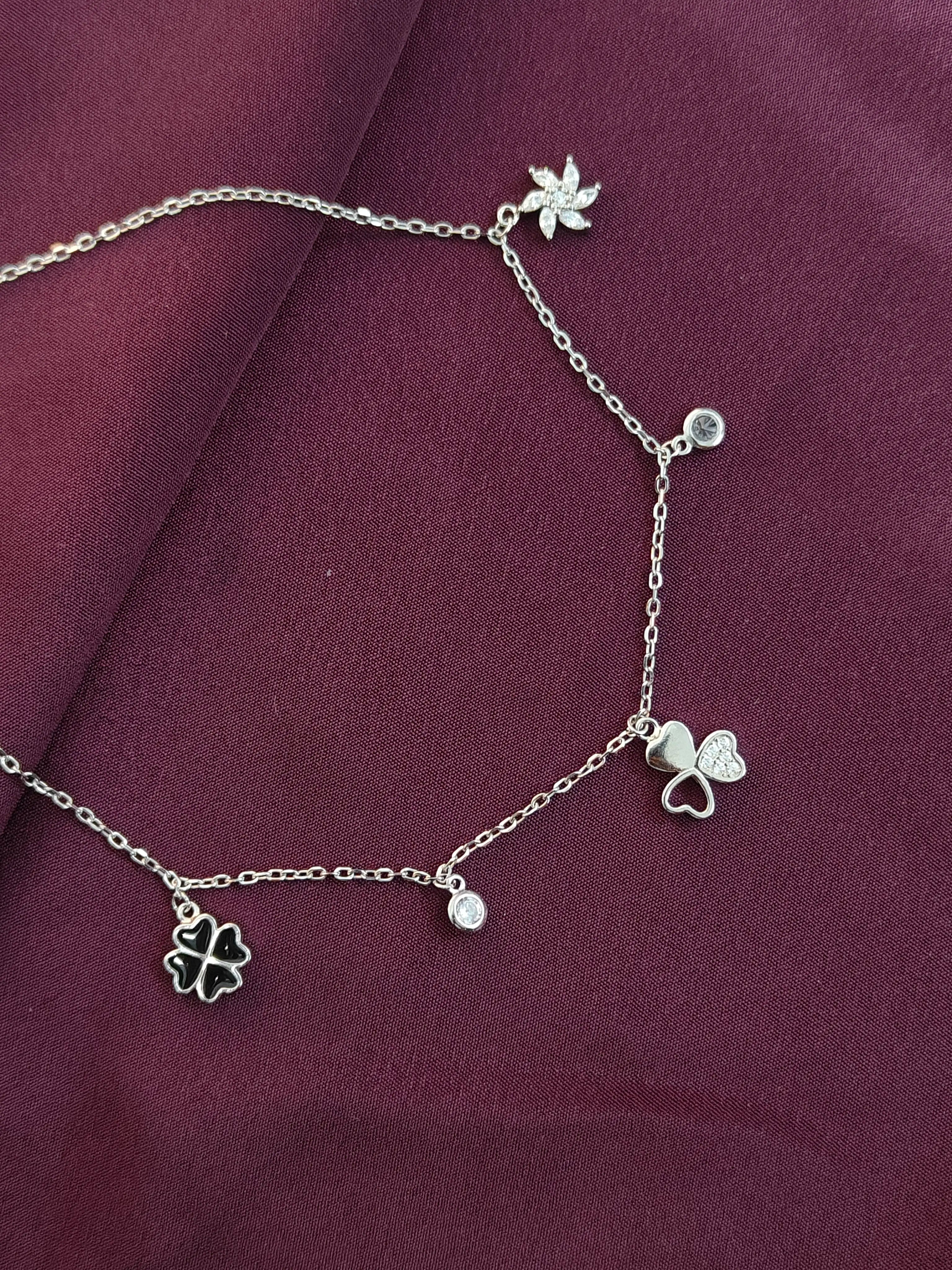 Silver anklet with charms on a purple fabric background